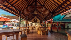 An open-air restaurant with wooden tables and chairs, a tiled floor, and a thatched roof. - Semaya One Beach Guesthouse (Penida Island)