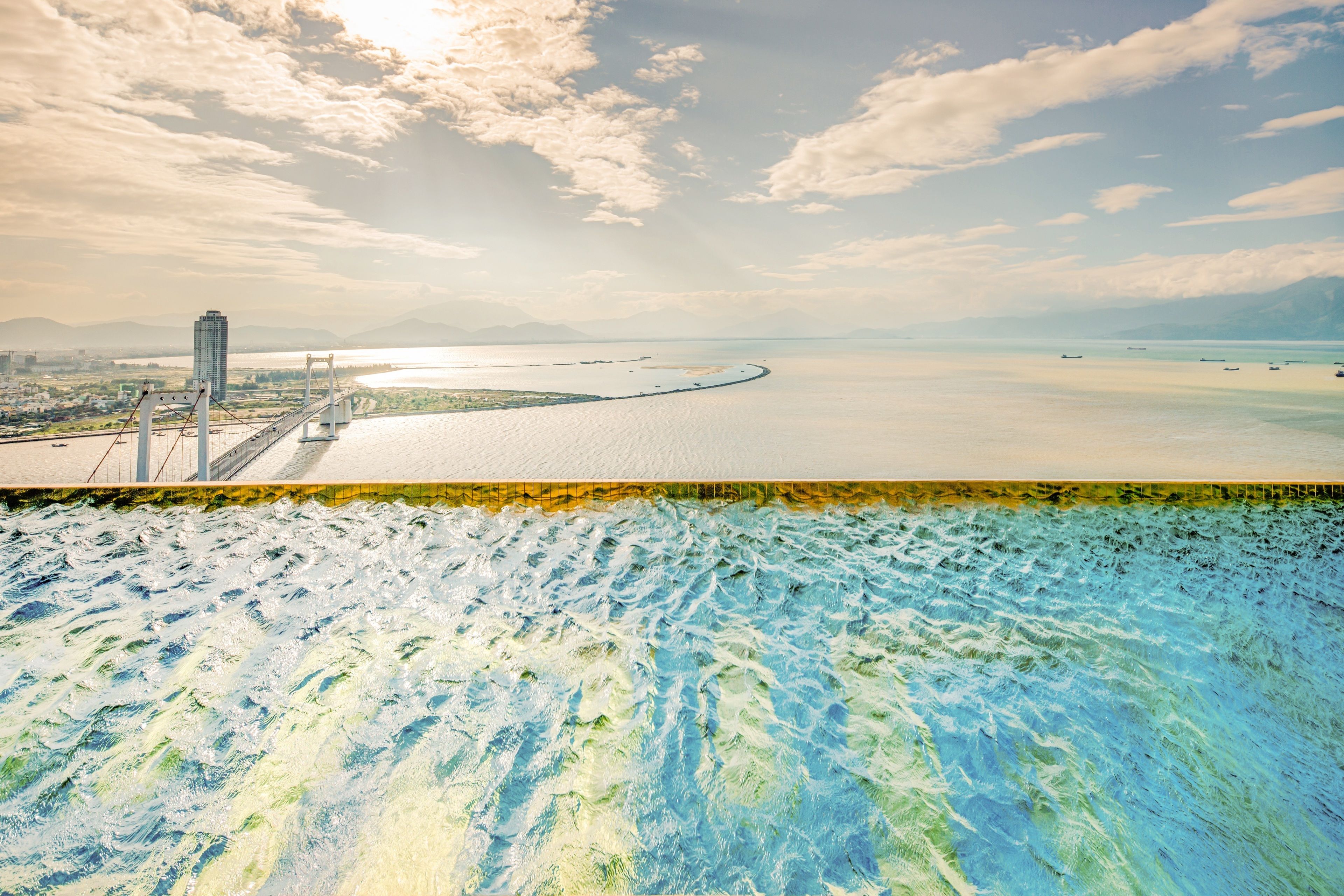 A coastal view with a bridge, a body of water, and a distant mountain range.