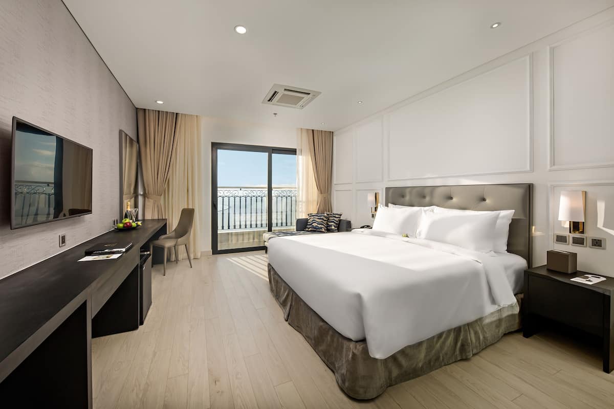 Quarto de hotel moderno com uma cama grande, uma escrivaninha, televisão e varanda com vista.