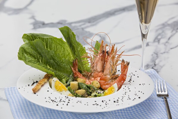 Un plato de comida con camarones, lechuga y otras verduras, acompañado de una copa de champán.