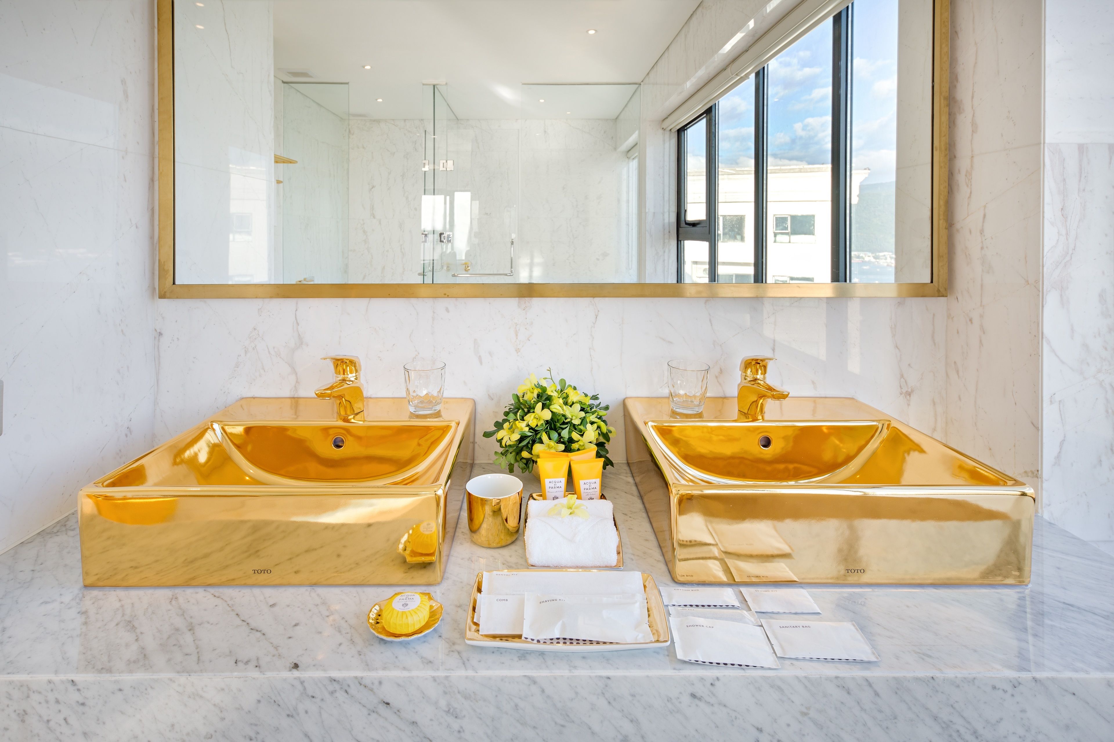 A luxurious bathroom with two gold sinks, a large mirror, and a view of the outdoors.