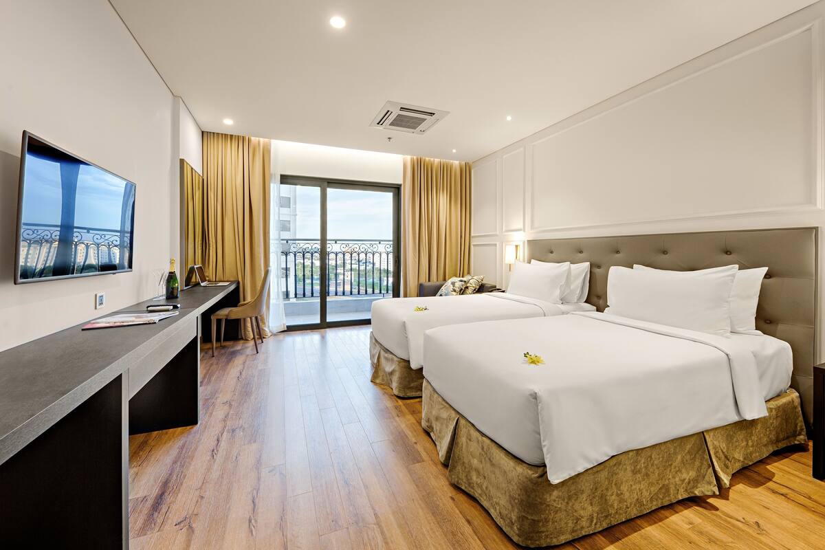 Quarto de hotel com duas camas, uma escrivaninha, televisão e varanda com vista.