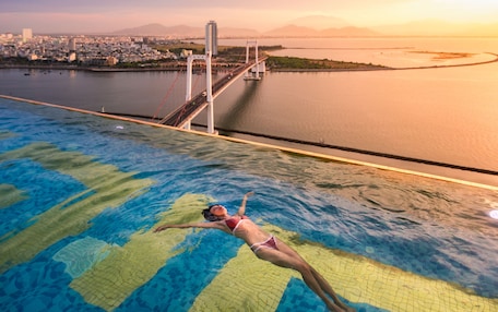 A person swimming in a pool with a cityscape and bridge in the background.