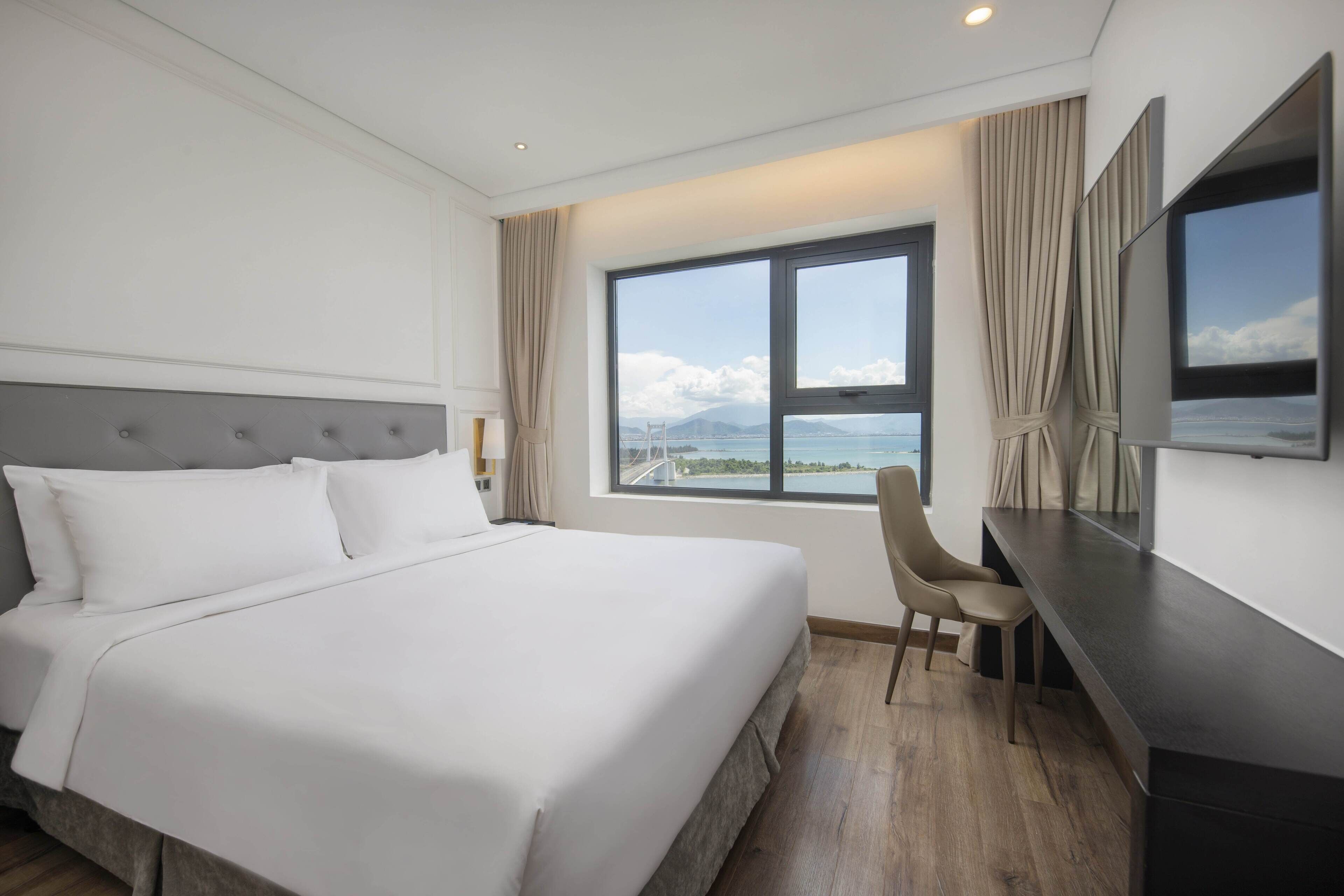 A hotel room with a large bed, a desk, and a view of the sea.