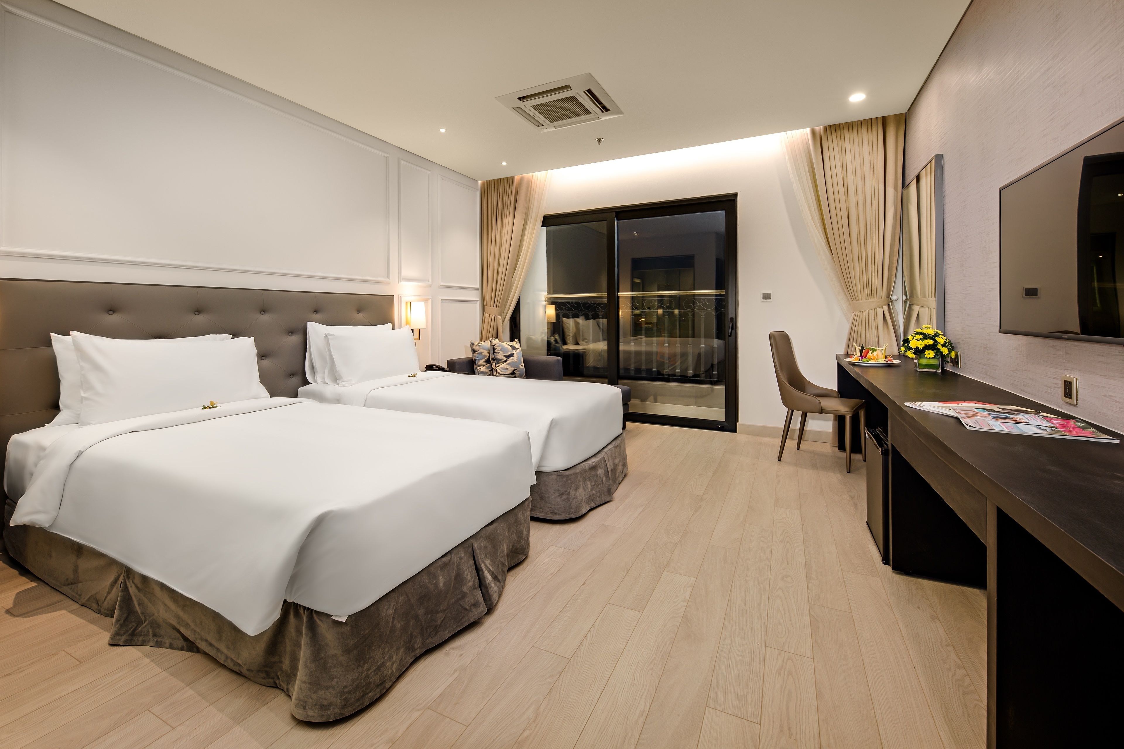 Een hotelkamer met twee bedden, een bureau, een stoel, een televisie en een schuifpui naar een balkon.