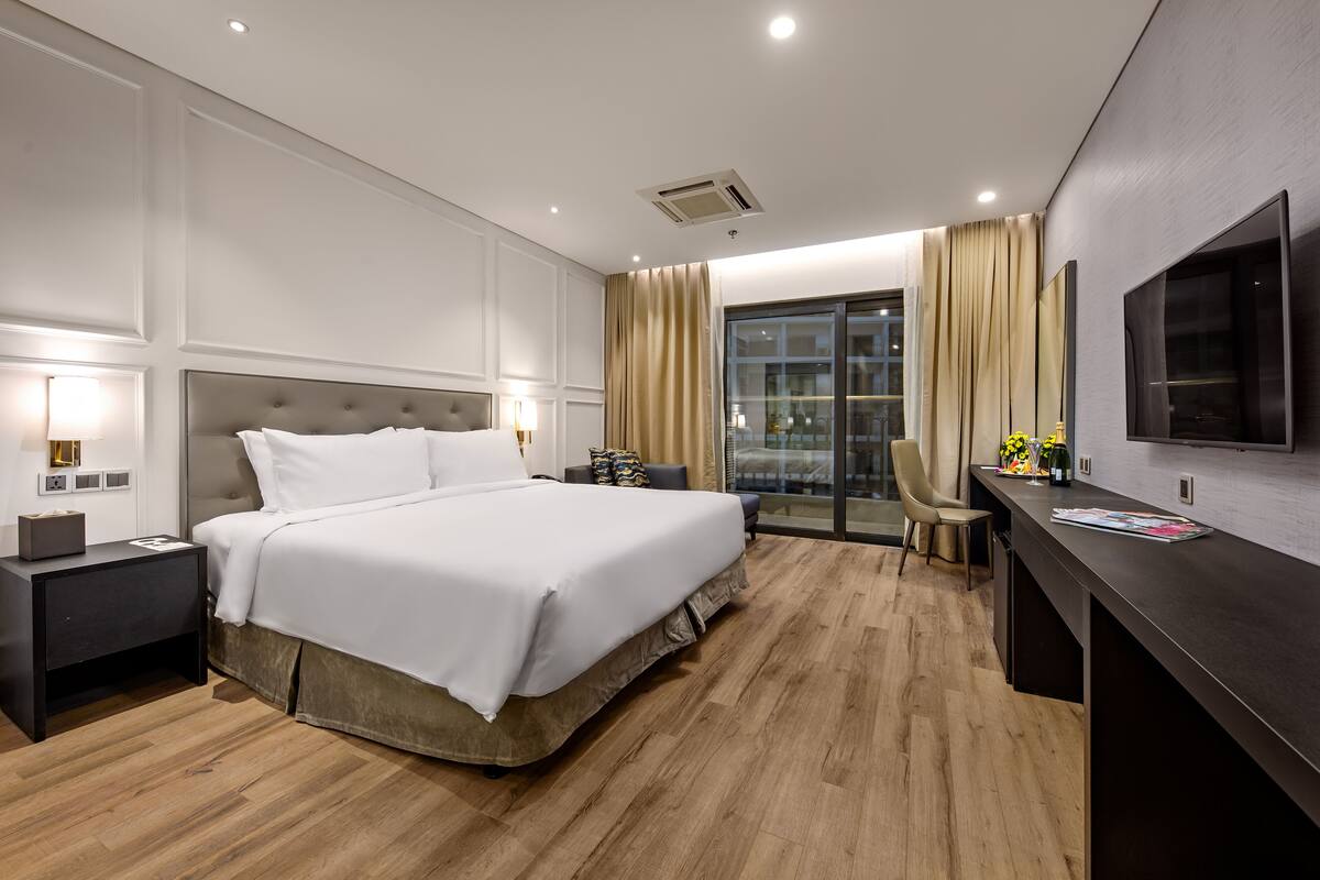 Quarto de hotel moderno com uma cama grande, uma escrivaninha, uma cadeira e uma televisão.