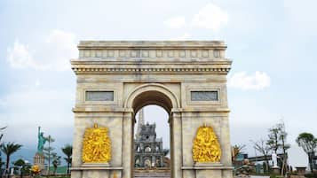A large stone archway with golden statues on either side, leading to a building with a tower in the background.