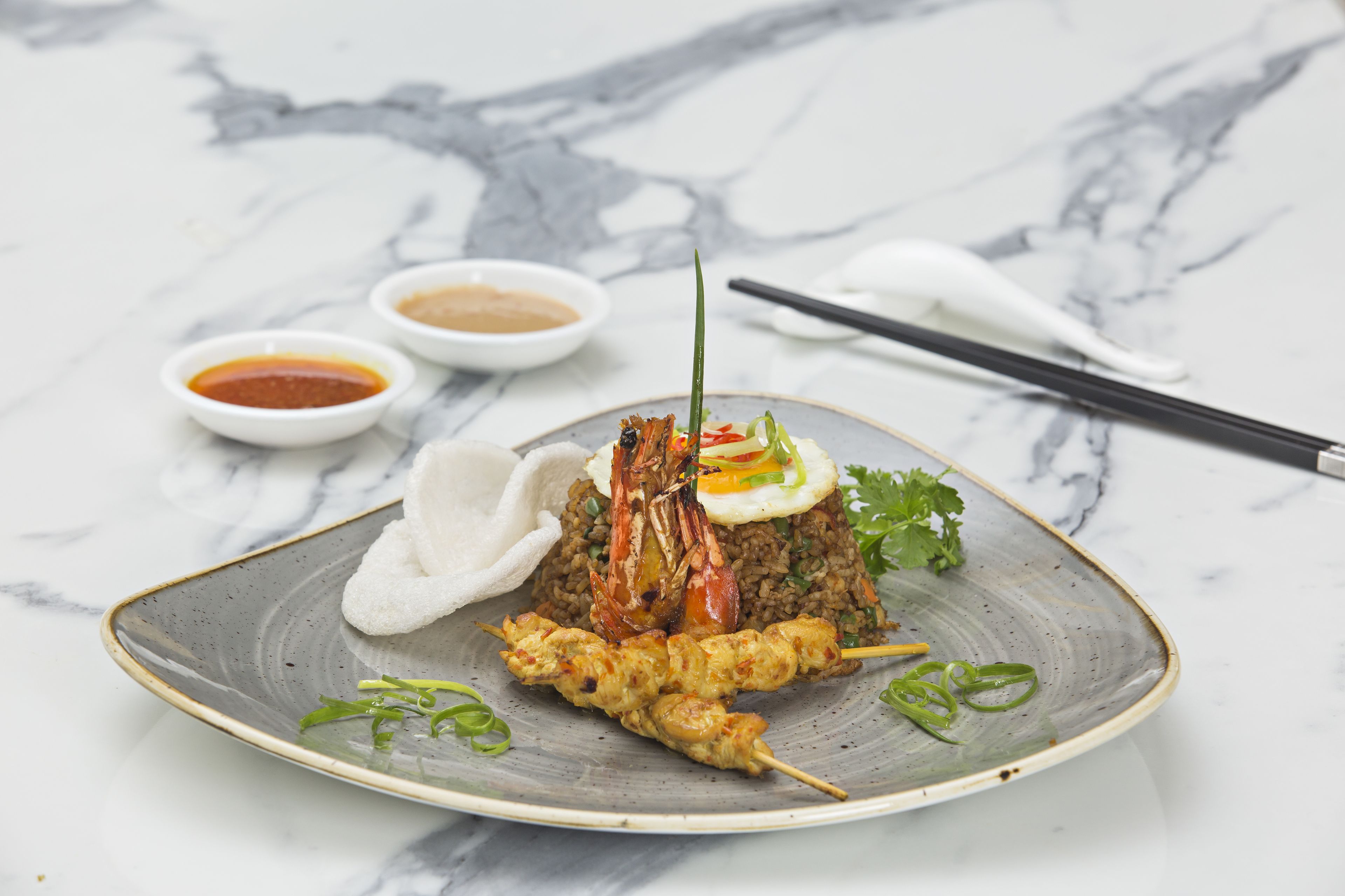 A plate of food with skewers and a mound of rice, accompanied by small bowls of sauce, on a marble surface.