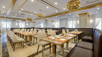 A conference room with multiple tables and chairs, a large seating area, and modern chandeliers.