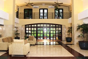 A spacious lobby with a high ceiling, two levels of balconies, and large windows offering views of greenery.