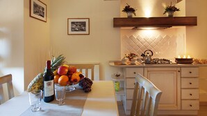 Een eethoek met een tafel gedekt voor twee personen, inclusief een fles wijn, een schaal fruit en een kaars.
