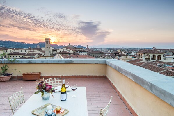 A rooftop terrace with a table set for dining, overlooking a cityscape at sunset. - La Culla di Dante Luxury Apartment in front of the Duomo (sleeps 6) (Firenze)