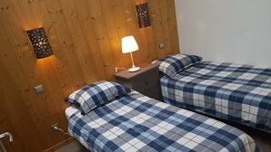 Una stanza con due letti, ognuno con copriletto a quadretti blu e bianchi, un comodino con lampada e una parete in legno con due applique.