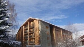 Un edificio in legno a più piani con balconi, circondato da alberi innevati.