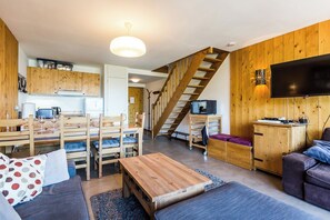 Ett modernt vardagsrum med matplats, soffa, soffbord, TV och en trappa.