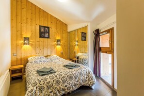 A bedroom with a wooden wall, a bed with a patterned bedspread, two bedside tables, and a window with curtains.