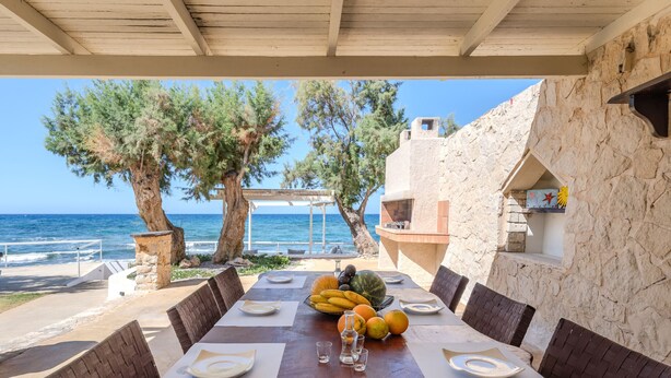 Mesa para dos personas dispuesta con vista al mar, rodeada de muros de piedra y mobiliario de madera.