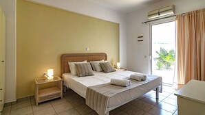 Una habitación de hotel con cama, mesitas de noche, ventana con cortinas y un equipo de aire acondicionado.