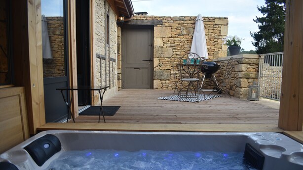 Een hottub met een houten terras, stenen muren, een deur en tuinmeubilair.