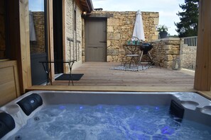 Een hottub met een houten terras, stenen muren, een deur en tuinmeubilair.