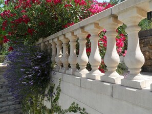 A stone balustrade with a series of balusters, surrounded by lush greenery and vibrant flowers.
