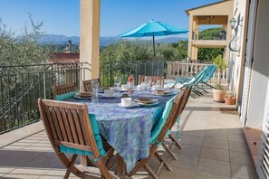 An outdoor dining area with a table set for four, surrounded by chairs, on a balcony with a view of the countryside.