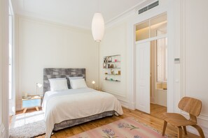 A bedroom with a bed, bedside table, lamp, and a chair.