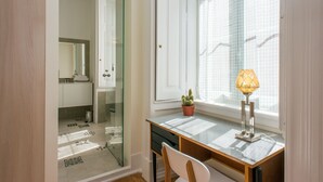 Une salle de bain avec une porte de douche en verre, un lavabo et un cactus en pot posé sur le rebord de la fenêtre.