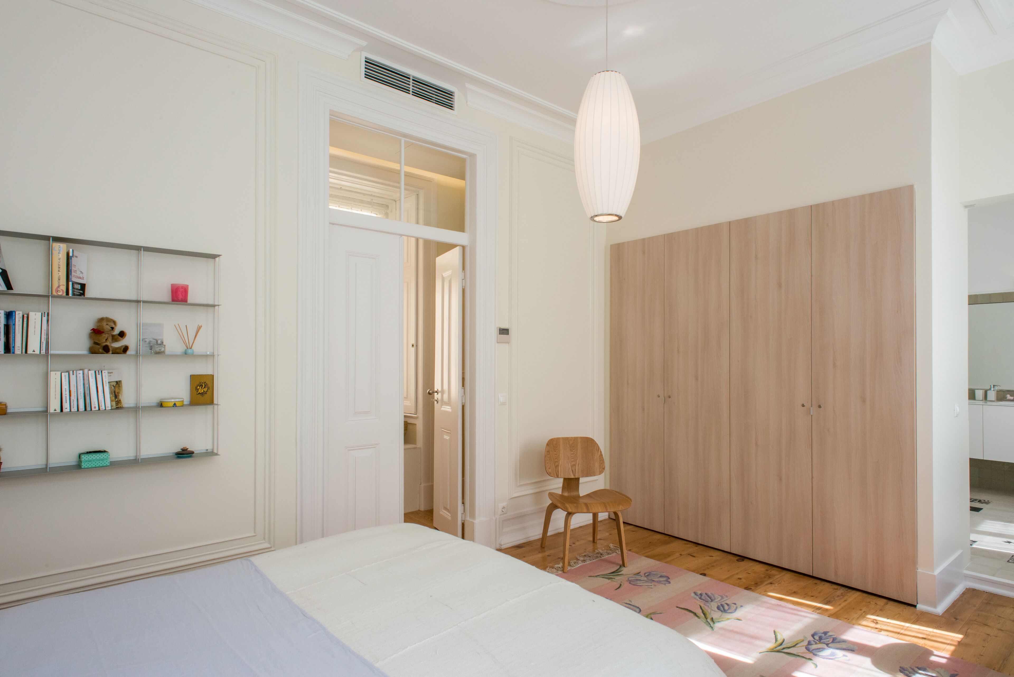 A bedroom with a bed, a wooden wardrobe, a bookshelf, and a chair.