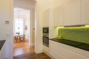 A modern kitchen with white cabinets, a black countertop, and a green backsplash.