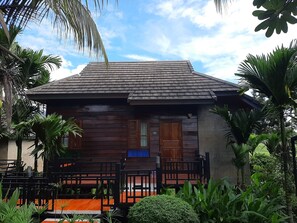 A wooden house with a tiled roof, surrounded by lush greenery and palm trees. - Buraphat Resort (Chiang Dao)