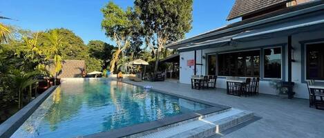 A swimming pool with a patio area, outdoor seating, and a building with large windows.