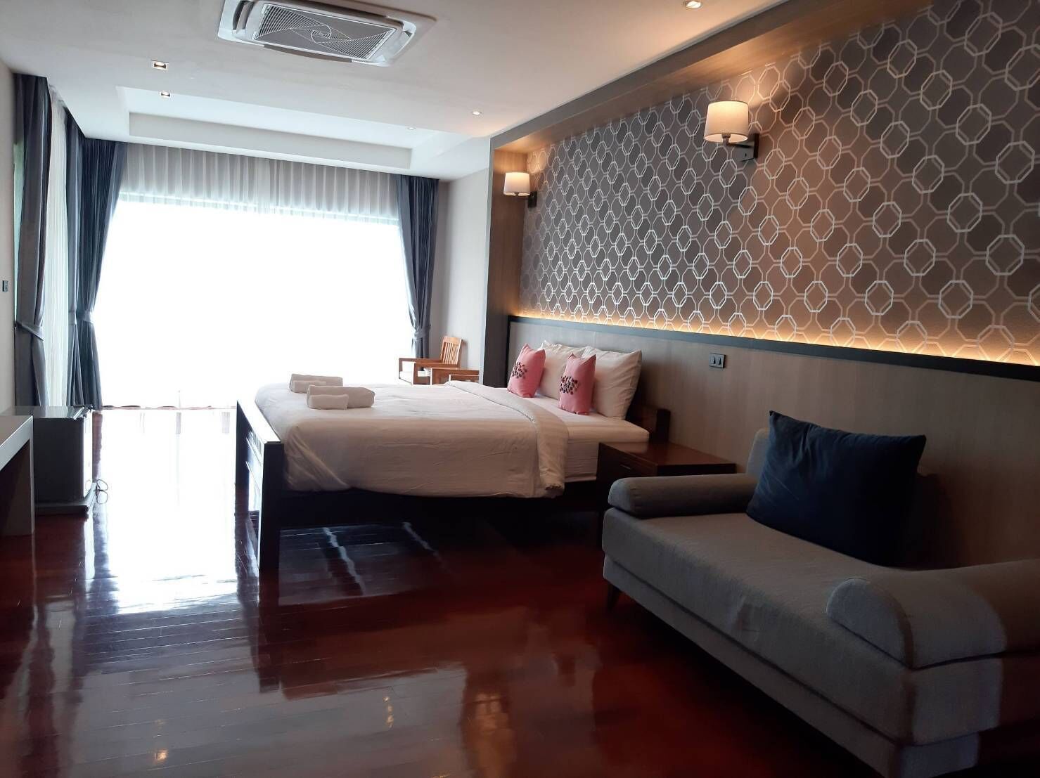 A hotel room with a bed, a sofa, a wall with a geometric pattern, and a window with curtains.