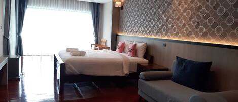 A hotel room with a bed, a sofa, a wall with a geometric pattern, and a window with curtains.