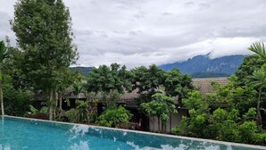 A swimming pool with clear water, surrounded by lush greenery and a mountainous backdrop.