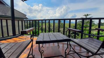 A wooden deck with a table and two chairs, overlooking a lush landscape.