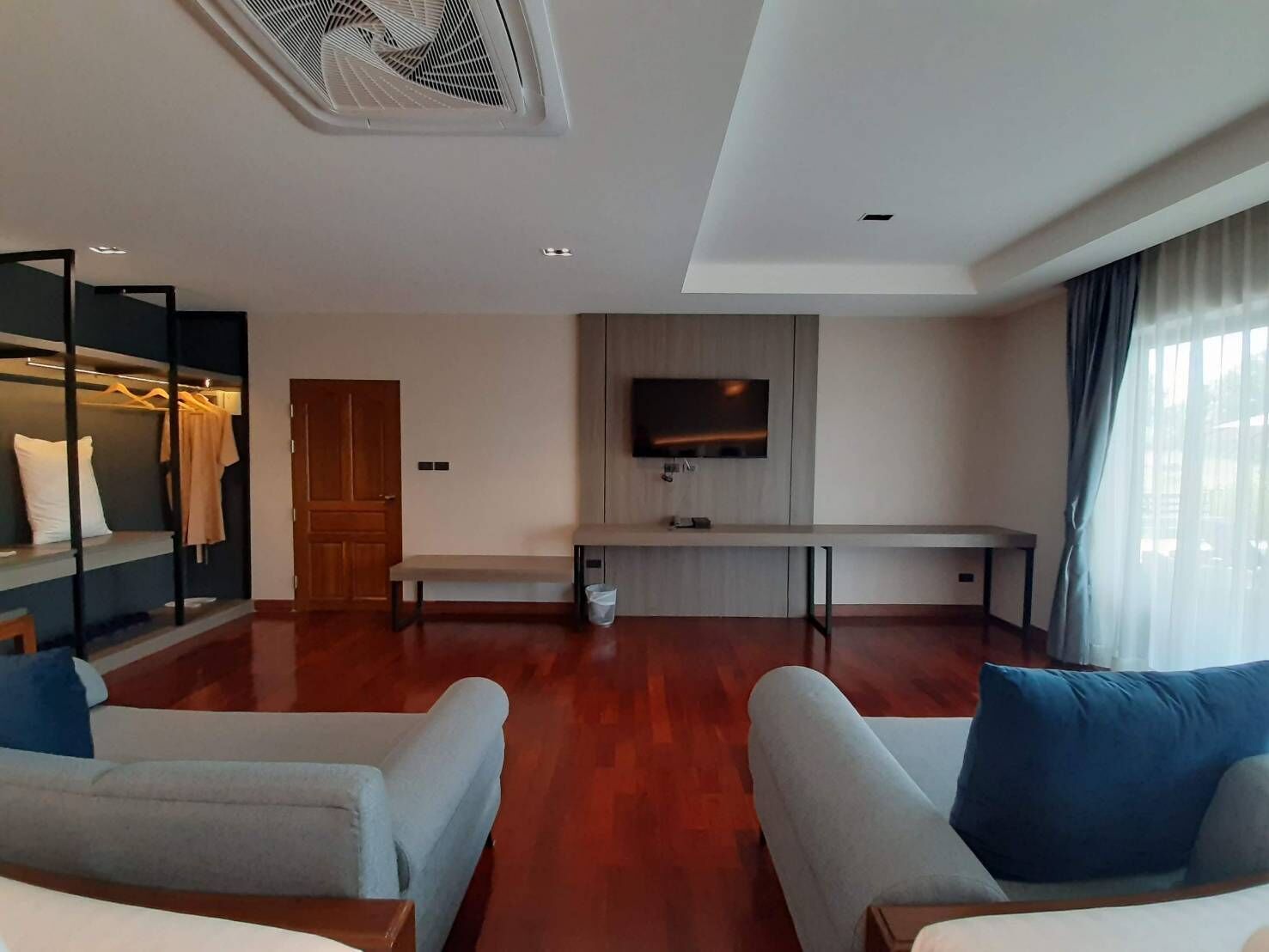 A modern living room with a flat-screen TV, a bench, and a clothing rack.