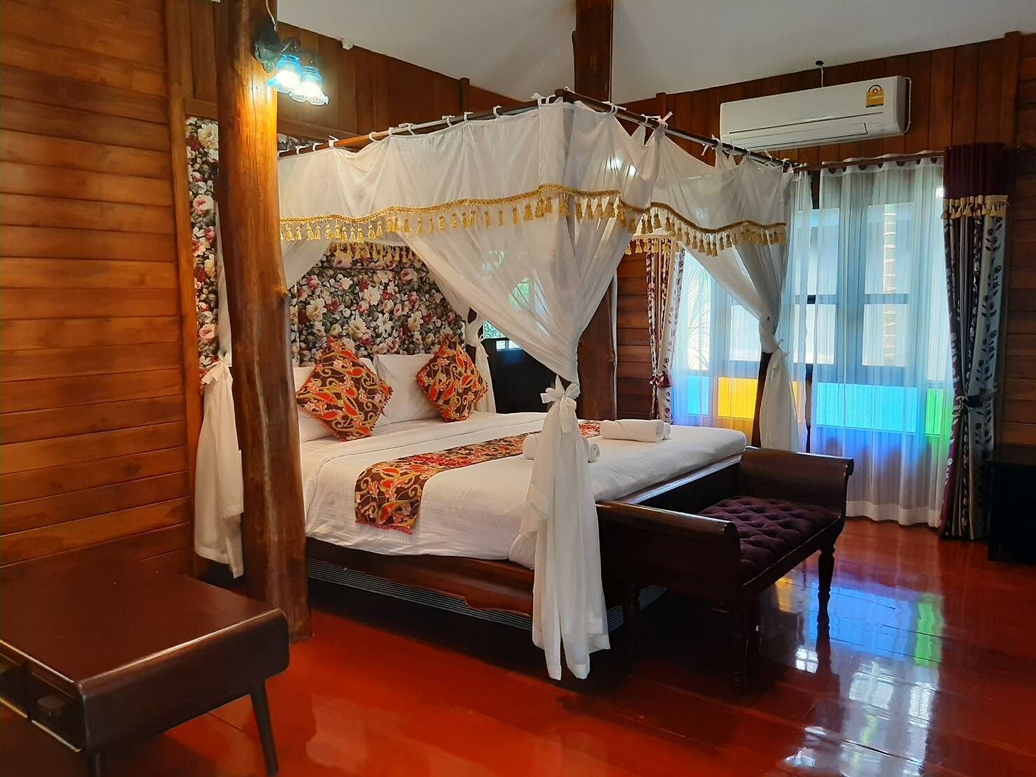 Una cama con dosel, un banco de madera y un cabecero floral.