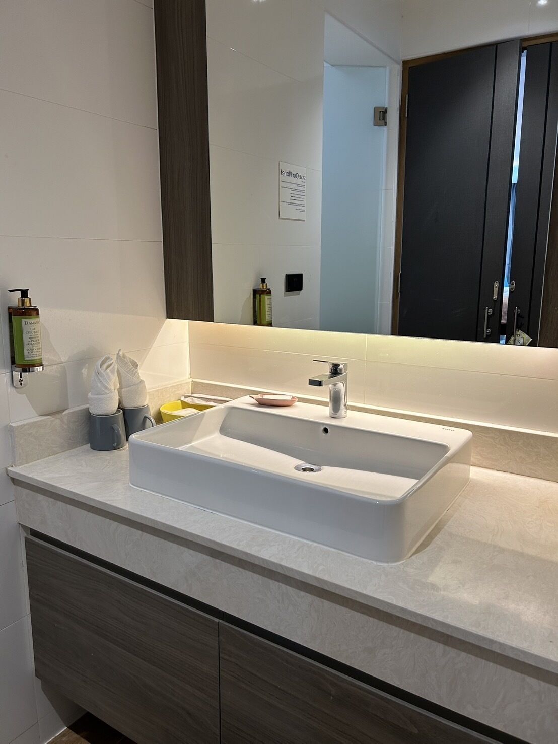 A modern bathroom with a large rectangular sink, a mirror, and a dark wooden door.