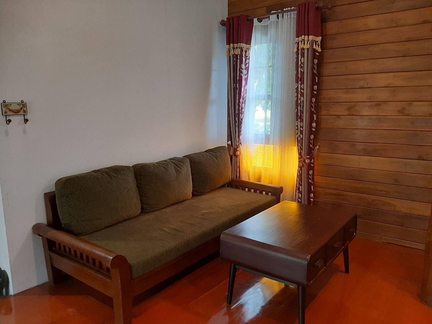 Un plancher en bois, un canapé, une table en bois et une fenêtre avec des rideaux.