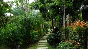 A wooden deck leading to a garden with a stone pathway, lush greenery, and a small waterfall.