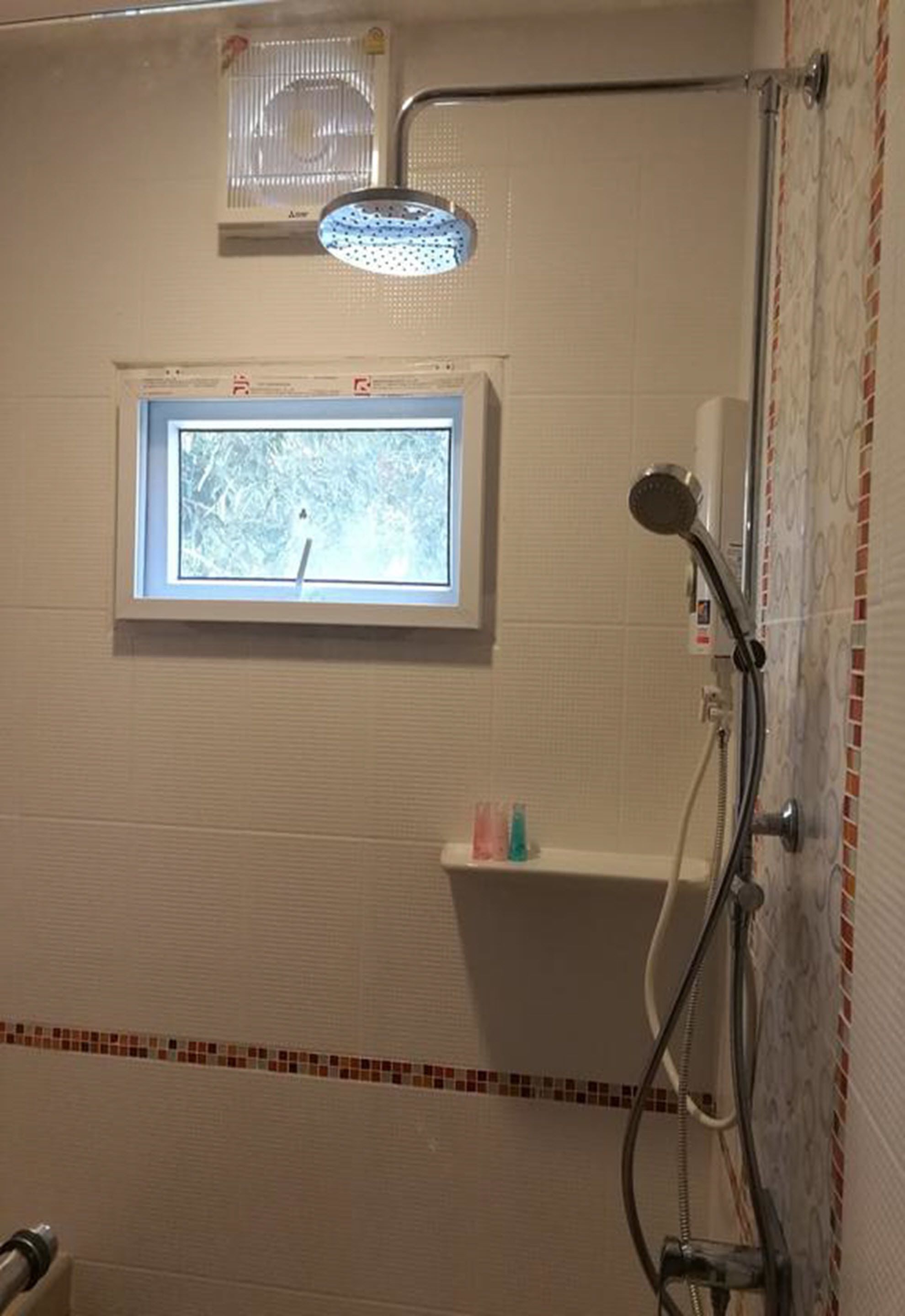 Un espace douche avec une fenêtre, une étagère pour les articles de toilette et un pommeau de douche.