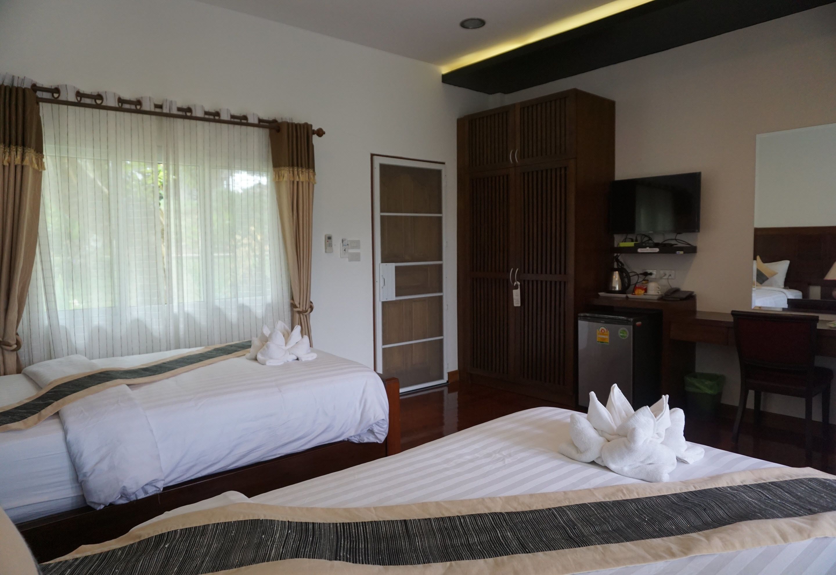 Een hotelkamer met twee bedden, een bureau, een televisie en een kledingkast.