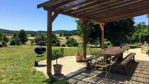 An outdoor patio with a wooden pergola, a barbecue grill, a table, and chairs. - Farmhouse for 15 people, swimming pool, SPA, billiards, air conditioning (Luzy)