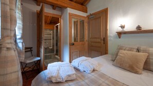 Een slaapkamer met een bed, twee witte handdoeken, een houten stoel en een houten plankje met een dennenappel.