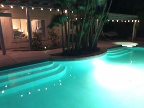 A swimming pool with a curved edge and a light blue tint. There are palm trees and a building with a porch in the background. - VILLA VILLETA PARADISE! 4 BDRM+BONUS RM, 4 HOLE GOLF, PEBBLE POOL #103548 (La Quinta)