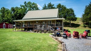 Un chalet doté d’un porche couvert, de meubles d’extérieur et, en arrière-plan, d’une grange rouge.