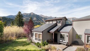 Ein zweistöckiges Haus mit einer Veranda, einem Vorgarten und Bergen im Hintergrund.