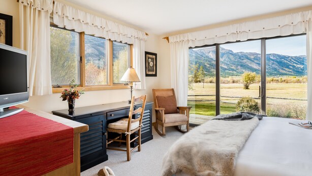 Ein Schlafzimmer mit Bett, Schreibtisch, Stuhl, Fernseher und großen Fenstern mit Blick auf die Berge.