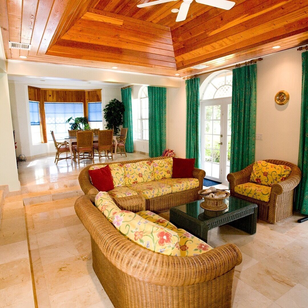 A spacious living area with a high ceiling, wicker furniture, and green curtains.